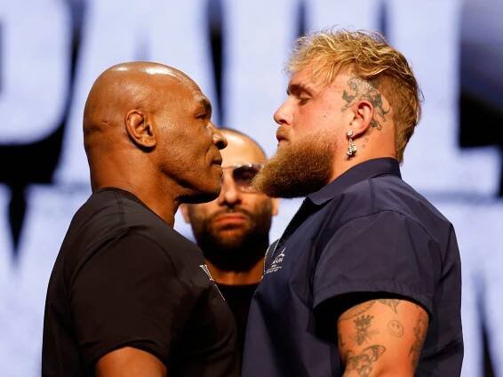 Mike Tyson and Jake Paul stand chin to chin at a preview event for their boxing match, Tyson in a black shirt and Paul with a long beard wearing navy blue.