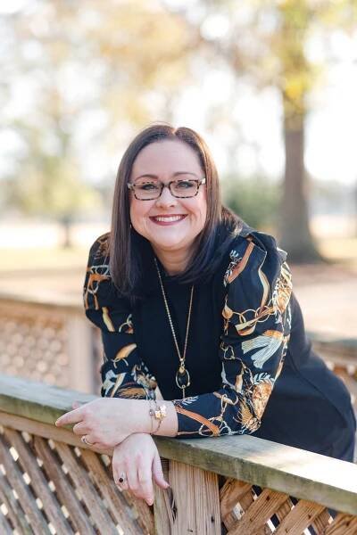 Amanda Jones, fair skinned woman with dark hair and classes leaning forward and smiling. 