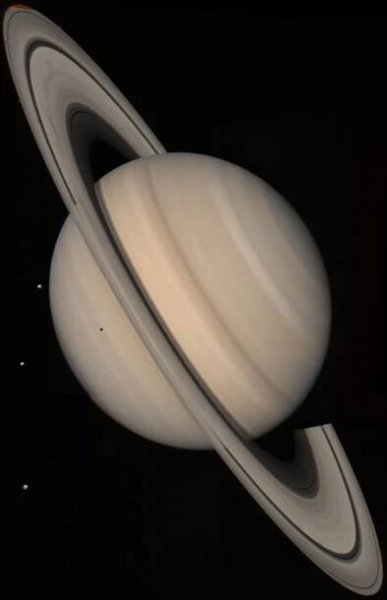 Saturn appears pale beige and yellow with its rings encircling it. Three small white dots appear off the left of the planet. These are three of Saturn's moons.