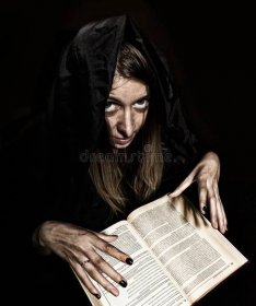 Pretty witch casts spells from thick ancient book by candlelight on a dark background royalty free stock image