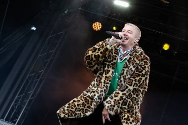 Macklemore in a cheetah fur coat and green shirt rapping onstage