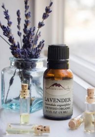 Amber bottle of organic lavender essential oil with small vials and lavender flowers in background
