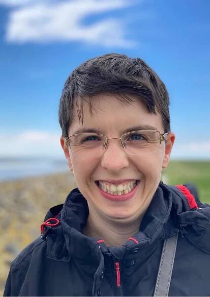 Eine junge Frau mit kurzen Haaren, Brille und dunkelblauer Windjacke