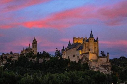 Alcázar of Segovia castle at dusk, with streaks of pink and purple against a predominantly blue sky.