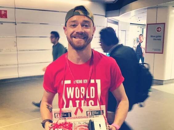 Man stands in red World Aids day top smiling 