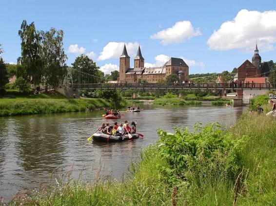 Auf einem Fluss sind Paddelboote mit Menschen drauf zu sehen.