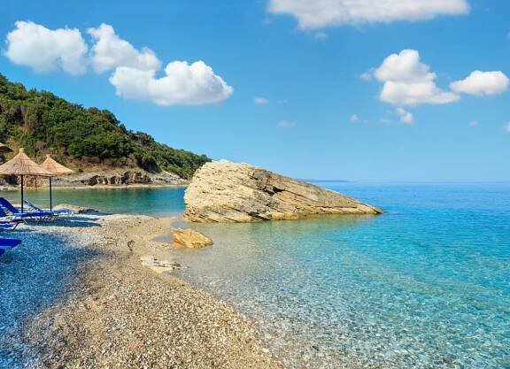 Letní ráno Pulebardha pláž s lehátky, slámově slunečníky a oblázkové (Sarandë, Albánie). — Stock obrázek