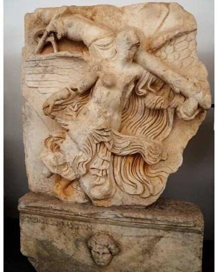 Fig. 2. Panel C9: Nike with trophy. Museum of Aphrodisias.  ot only did the Sebasteion celebrate the victory and virtus of Augustus, but also of he subsequent Julio-Claudian emperors. The victory of the emperors is the subject of Panel C9 from the south building (Fig. 2). A semi-nude Nike majestically flies across the panel, carrying over her left shoulder a robust tropaeum. The base of the relief contains he inscription NEIKH XEBAXTON, or “the victory of the emperors.” Constructed on a knotted tree trunk, the trophy is composed of a plain cuirass with a simple skirt, a sword in its scabbard attached with a ribbon, and a helmet with a plume. That the trophy  