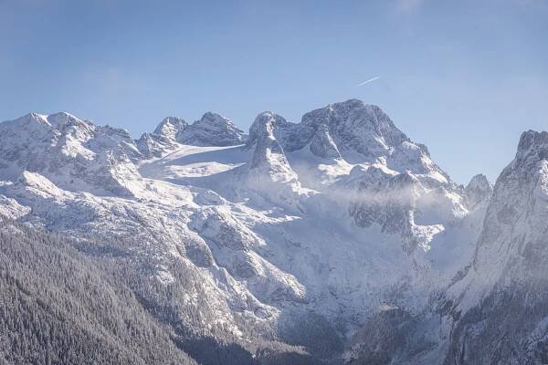Blick auf den schneebedeckten Dachstein Geltscher mit markanten Gipfeln, umgeben von einem verschneiten Wald unter einem strahlend blauen Himmel.