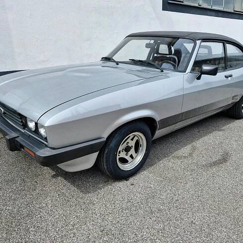 Ein silberner Ford Capri parkt vor einem weißen Gebäude.