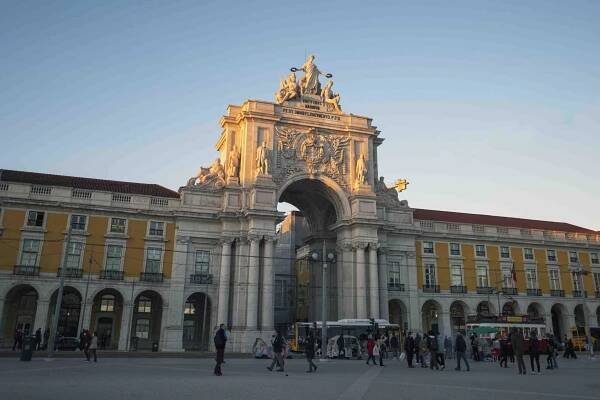 A large white arc with pillars, and yellow buildings on either side in Lisbon, Portugal