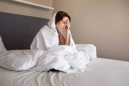 Mladá žena sedící v posteli zakrytý peřinou se drží zoufale za hlavu, protože nemůže usnout