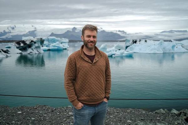 Matthew Rigby in front of glacial ice formations and icy landscapes at Jokulsarlon glacial lagoon in Iceland.
