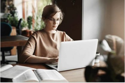 Work, lifestyle and business concept. good-looking focused european female in trendy glasses sitting in cafe near laptop, working on notebook, surrounded with books, making notes.
