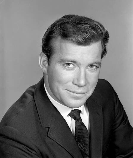 Person in a suit with slicked-back hair, smiling slightly at the camera
