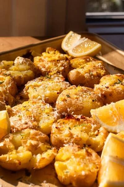 side view shot of the baked smashed potatoes on a sheet pan with lemon wedges on the pan 