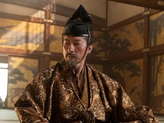hiroyuki sanada as yoshii toranaga, a man wearing ornate golden clothing and an eboshi headpiece, sitting alone in a room crosslegged