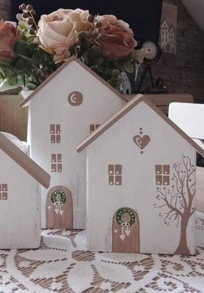three wooden houses are sitting on a table with flowers in the vases behind them