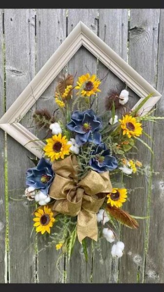 a bouquet of sunflowers and cotton in front of a wooden wall with a frame