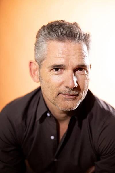 A man with greying hair smiles slightly.