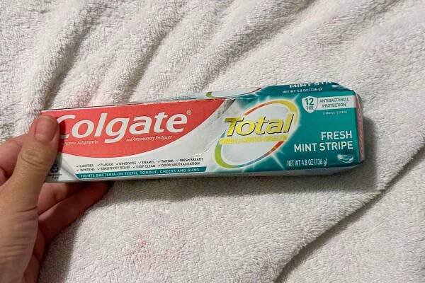 A hand holding the Colgate Total Fresh Mint Stripe Gel Toothpaste box on a towel