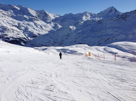 a person standing on top of a snow covered slope next to a fence and mountains