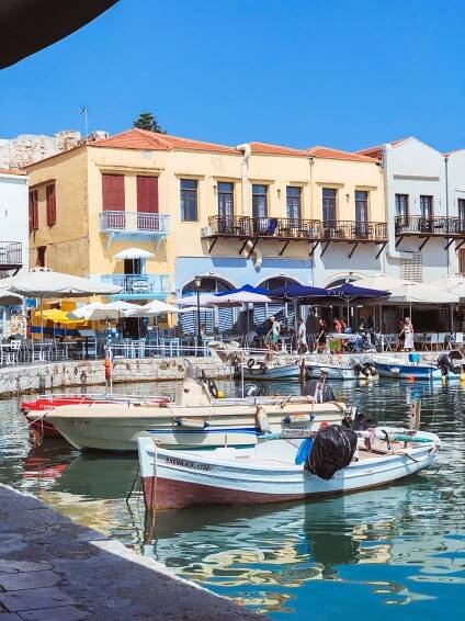 Scenic view of Rethymno’s Old Harbor in Crete with colorful fishing boats and historic waterfront buildings under a clear blue sky.
