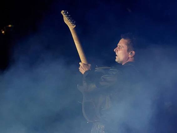 Matt Bellamy standing amongst smoke and holding his guitar neck upright