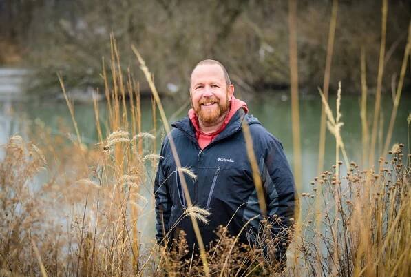 Photo of Michael Ward standing in tall grass on a riverbank.