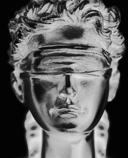 A metallic, blindfolded bust of a person is shown against a black background, symbolizing justice, impartiality, and the resolve to turn the other cheek in the face of adversity.