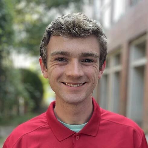 man with blonde hair wearing a red polo and smiling