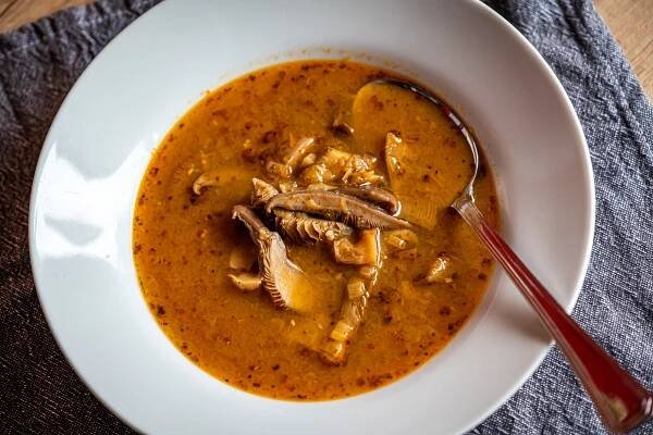 a white bowl filled with soup on top of a wooden table next to a red spoon