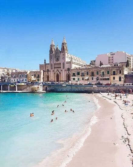 people are swimming in the clear blue water near an old church and beach on a sunny day