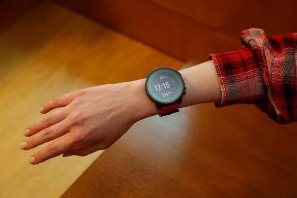 Suunto Vertical Titanium Solar am Handgelenk einer Frau. Im Hintergrund ist Holz zu sehen. Die Frau trägt eine rot weiß karierte Bluse