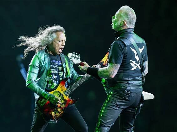 Kirk Hammett and James Hetfield of Metallica, captured on stage playing their guitars as they stand facing each other.