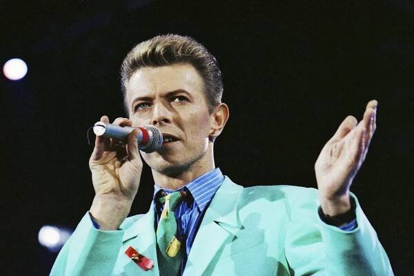 Man in blazer holding up microphone and singing at a concert.