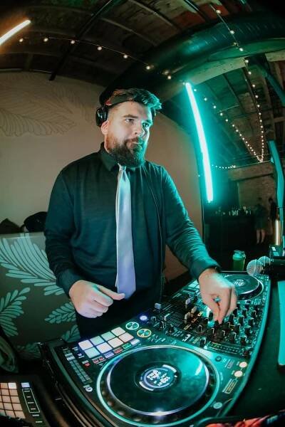 DJ performs at nightclub with professional equipment under moody green lighting and string lights overhead.