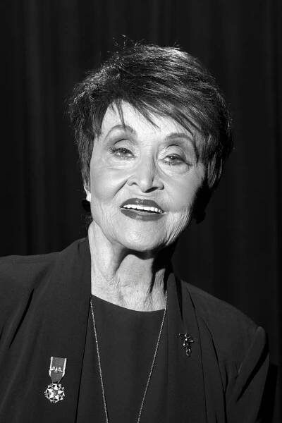 A black and white portrait of Chita Rivera, who is wearing a black blouse under a black blazer.