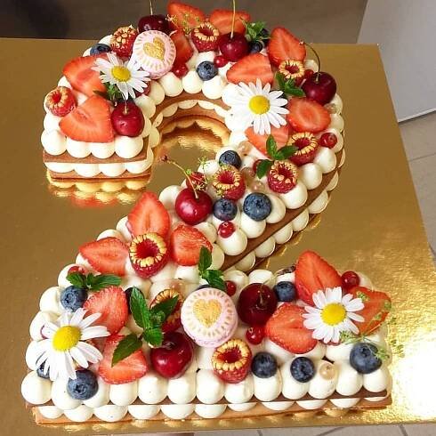 the number two is made up of fruit and flowers on a gold cake plate with white frosting