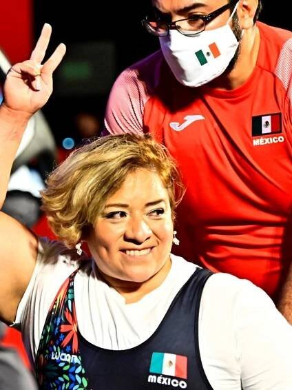 A woman smiling and raising her arm in a wheelchair chair being pushed by a man