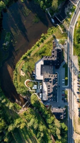 Aries Hotel & Spa Visla Exteriér fotografie An aerial shot captures a modern, multi-unit building complex nestled beside a winding river. The buildings are predominantly dark gray or black with flat roofs and some with angled sections. They appear to be constructed with a contemporary architec