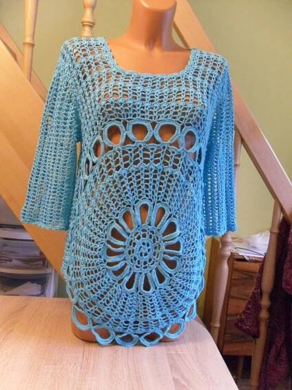 a blue crocheted top sitting on top of a wooden table next to a stair case