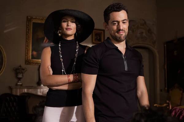 Gemma Arterton wearing a black hat stands next to Luis Gerardo Méndez.
