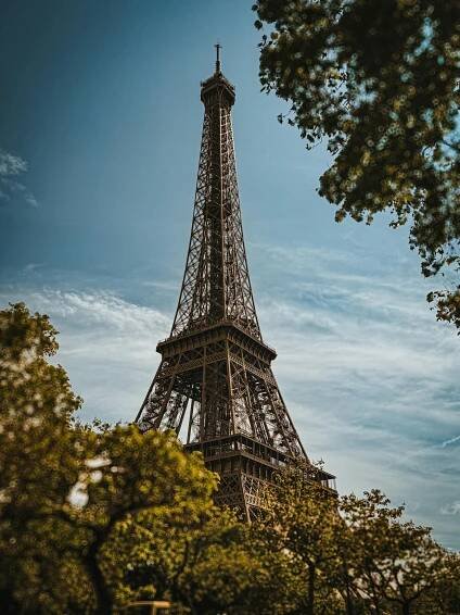 Free Striking low angle shot of the iconic Eiffel Tower framed by lush green trees and a clear sky. Stock Photo