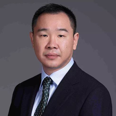 Gilbert Li, CFA, CPA - A man in a dark suit and a patterned tie with a light blue shirt poses against a plain gray background. With short black hair and a neutral expression, he exudes the precision of bioanalytical development.