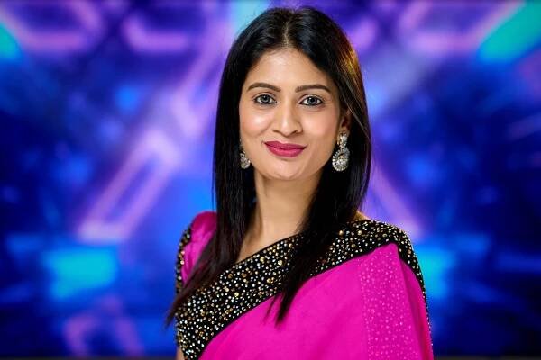 Professional portrait of person in bright pink sari with sequined details against purple background.
