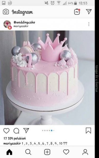 a pink cake with white icing and decorations on top, sitting on a table