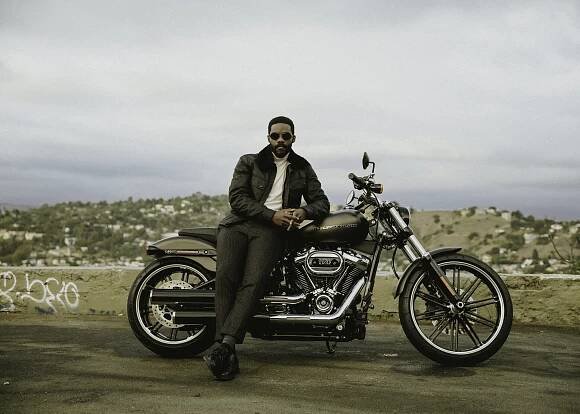 BELSTAFF jacket, ERMENEGILDO ZEGNA turtleneck, BALLY pants, DR. MARTENS shoes, and DIOR sunglasses.