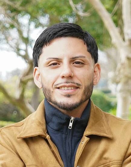 Dr Antonio with arms crossed in brown jacket smiling