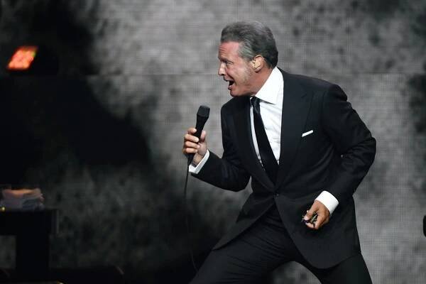 A photo of Mexican singer Luis Miguel performing during a concert in a black suit.